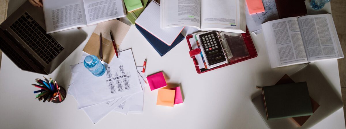 Students collaborate at a desk covered in open books, a laptop, and various study supplies.
